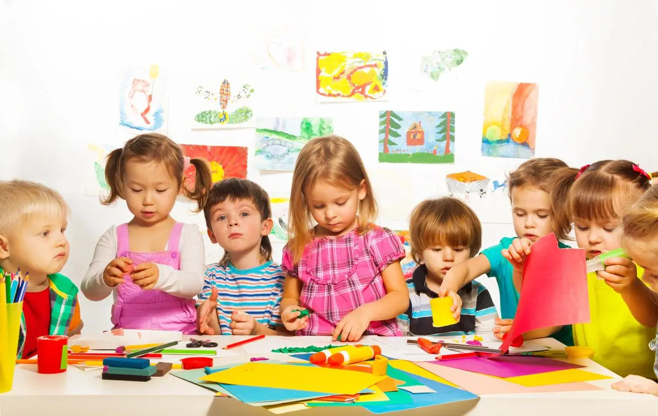 A group of children sitting at a table with some art supplies.