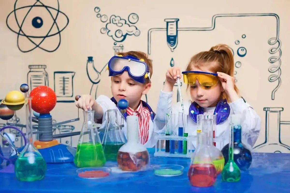 Two children in lab coats and goggles working with beakers.
